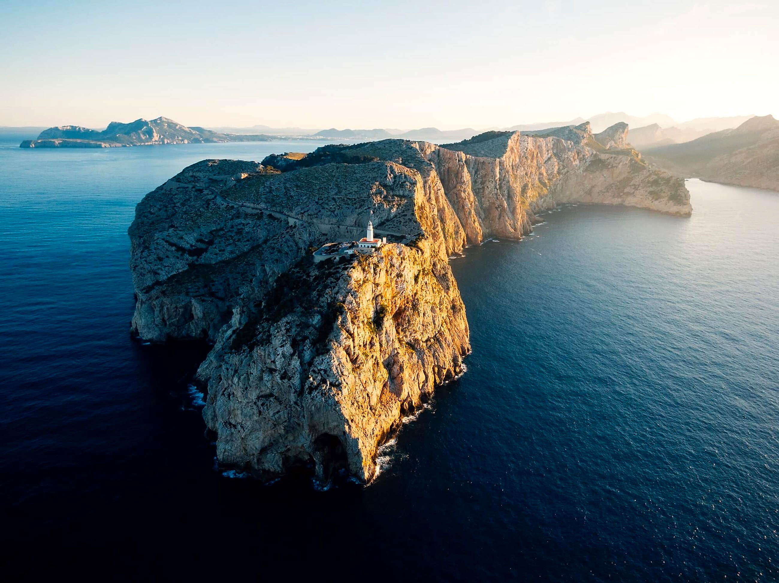 A white lighthouse tower rising from a rocky cliff above the ocean
