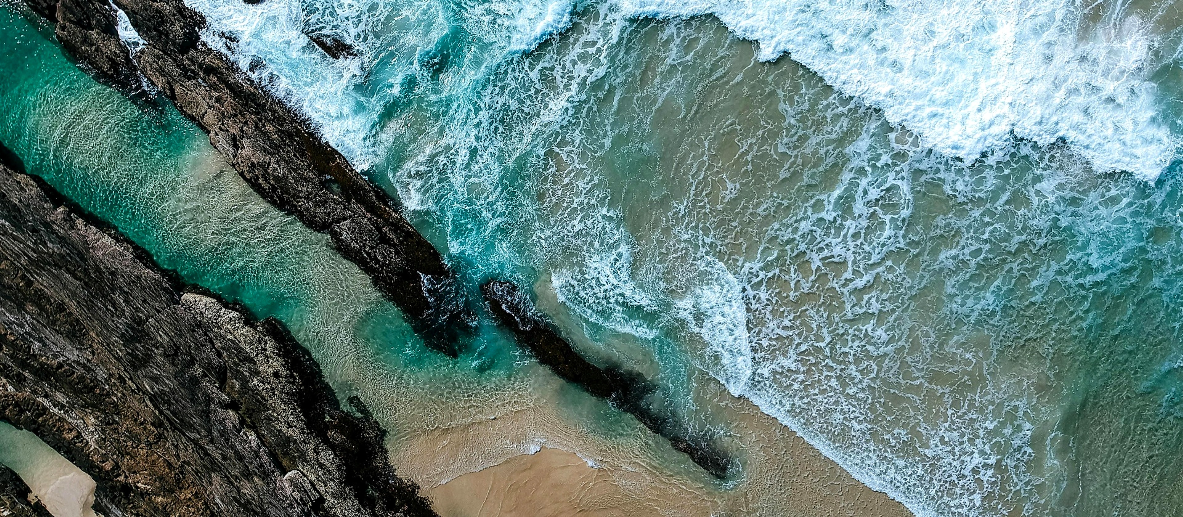 Aerial view of turquoise ocean waves washing over a rocky shoreline